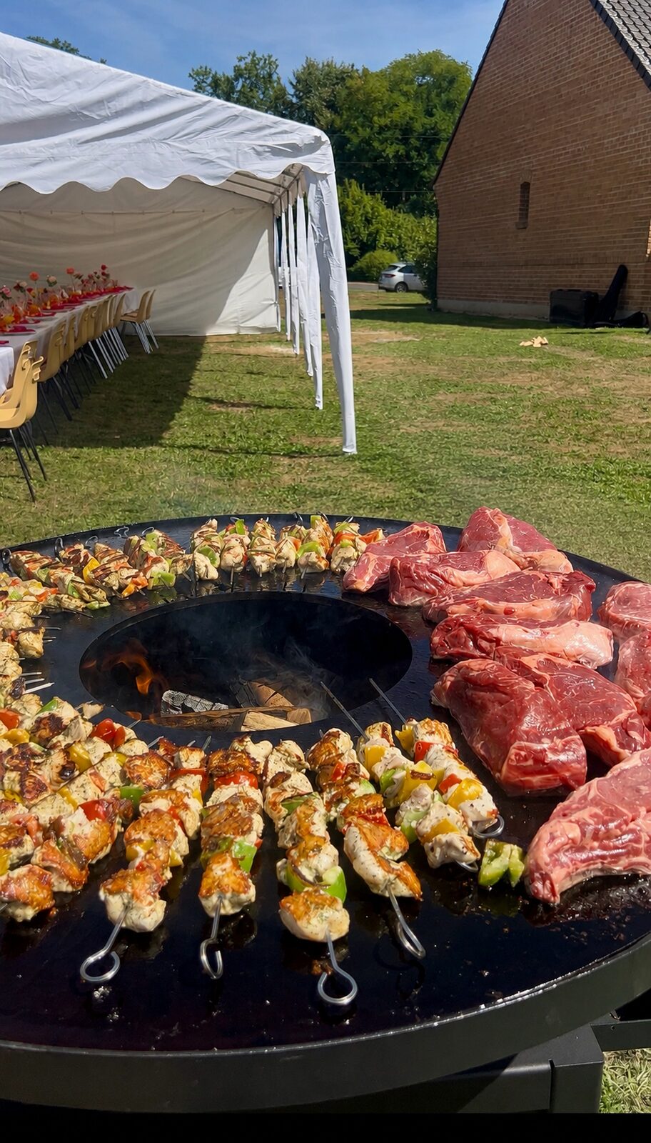 Brasero garni de brochettes et de pièces de bœuf devant un chapiteau de réception