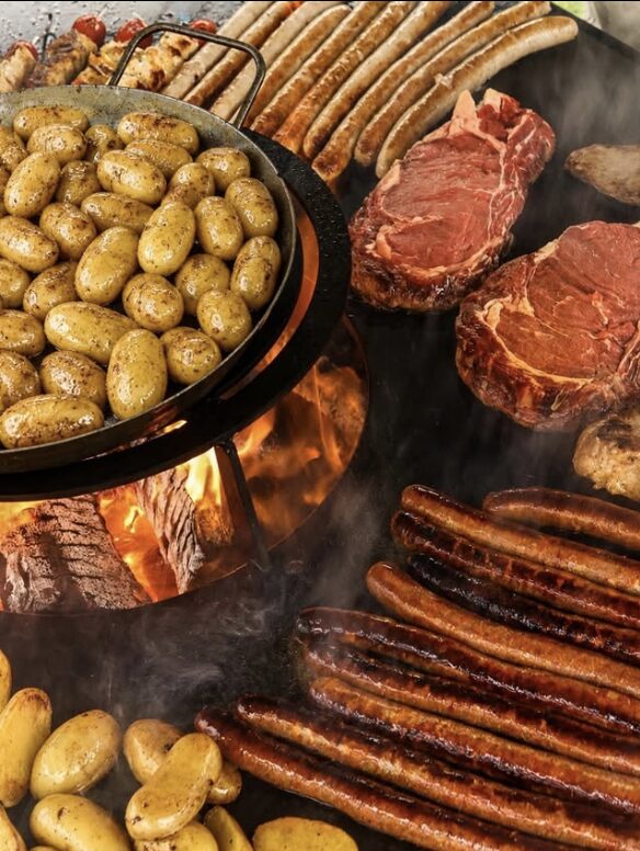 Grenailles dans une poêle au-dessus du foyer, côtes de bœuf en cuisson sur la couronne